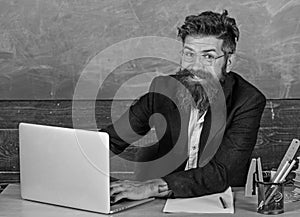 Back to school concept. Writing school report. Teacher bearded hipster with eyeglasses sit in classroom chalkboard