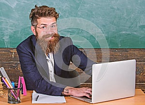 Back to school concept. Writing school report. Teacher bearded hipster with eyeglasses sit in classroom chalkboard