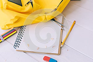 Back to school concept. Yellow backpack with notepad and stationery on a wooden background
