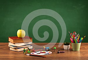 School items on desk with empty chalkboard