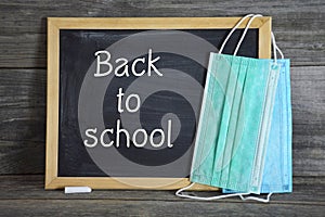 Back to school during corona virus pandemic. Blackboard and face masks on wooden background