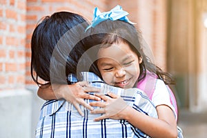 Cute asian pupil girl with backpack hugging her mother with happiness after back from school