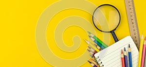 Back to school and education concept banner with notepad, color pencils and magnifying glass on the yellow table, top