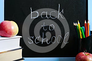 Back to school, education concept. Books, useful whole-grain cookies and apple on classroom table in front of blackboard.