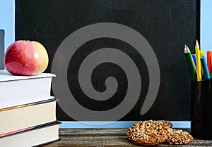 Back to school, education concept. Books, useful whole-grain cookies and apple on classroom table in front of blackboard.