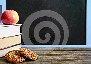 Back to school, education concept. Books, useful whole-grain cookies and apple on classroom table in front of blackboard.