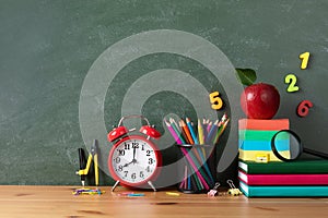 Back to school or education mockup with alarm clock, red apple and stationery supplies against blackboard on wooden table.