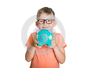 Back to school. Education and money concept. Portrait of smart little kid boy in glasses holding piggy bank and looking