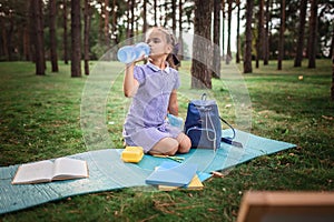 Back to school. Elementary scholars sitting on grass and drinking water during open-air class