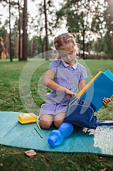 Back to school. Elementary scholars sitting on grass and packing books after open-air class