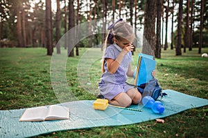 Back to school. Elementary scholars sitting on grass and wiping nose after open-air class