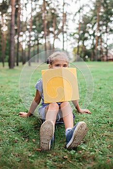 Back to school. Elementary school kid sitting on green grass with book at open-air class