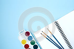 Back to school flat lay with watercolor, brushes and notepad on blue background