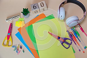 Back to school flatly. Top view on office, study supplies on light beige background. White earphones, colorful scissors, flower,