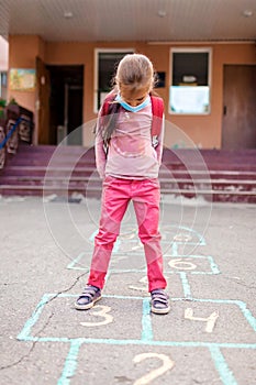Back to school. A girl in mask jumping and playing hopscotch before school building