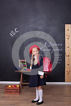 Back to school! A girl stands in school with a red backpack. Responds to the lesson. School concept. On the blackboard in Ukrainia