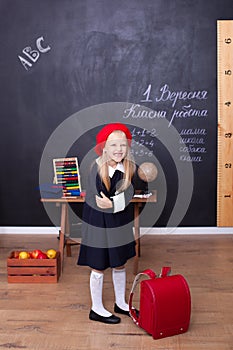 Back to school! A girl stands in school with a red backpack. Responds to the lesson. School concept. On the blackboard in Ukrainia