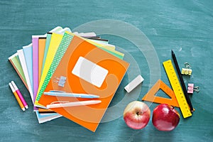 Back to school. Green blackboard with bright notebooks, pens, rulers, apples and scrapbook paper