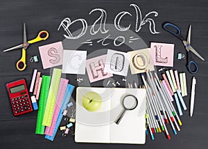 `Back to school` handwritten with school supplies on a black background. Top view.