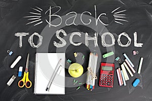 `Back to school` handwritten with school supplies on a black background. Top view.