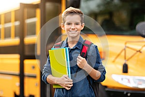 Back To School. Happy smiling preteen boy standing near school bus