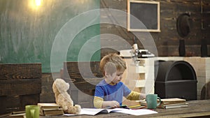 Back to school. Happy smiling pupil drawing at the desk. Child in the class room with blackboard on background. Teddy