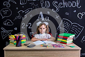 Back to school and happy time. Cute industrious child is sitting at a desk indoors with books, school supplies. Girl