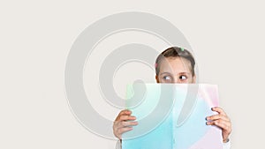 child girl holding a book in her hands with surprised looks out from behind the book