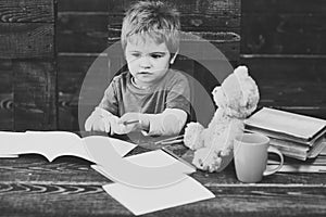 Back to school. Kid looking at copybooks on wooden table. Small concentrated boy holding colorful pencils