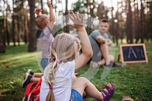 Back to school. Kindergarten and elementary scholars sitting with teacher on grass at open-air class