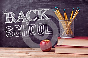 Back to school lettering with books, pencils and apple over chalkboard background