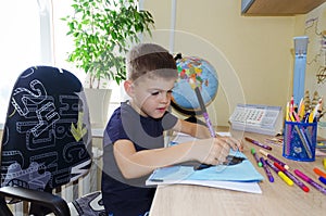 Back to school. Little tired boy doing homework at home with backpack full of books, pencils. Kid is drawing, writing and painting