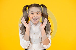 Back to school and looking delighted. surprised little girl smiling on yellow background. Small child with long brunette