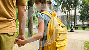 Back to school. Male parent and girl pupil of primary school go hand in hand