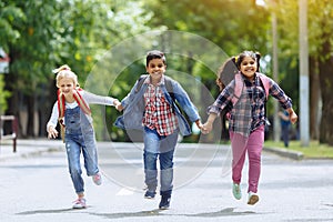 Back to school. Mixed Racial Group of happy elementary school students with backpacks running holding hands outdoors