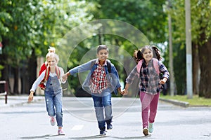 Back to school. Mixed Racial Group of happy elementary school students with backpacks running holding hands outdoors