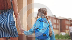 back to school. mom and daughter go to school view from behind with a backpack holding hands. kid education school