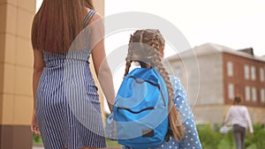 back to school. mom and daughter go to school view from behind with a backpack holding hands. kid education school