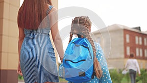 back to school. mom and daughter go to school view from behind with a backpack holding hands. kid education school