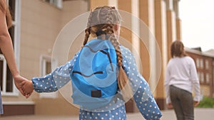 back to school. mom and daughter go to school view from behind with a backpack holding hands. kid education school