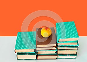 Back to school, pile of books in colorful covers and peach on wooden table with orange yellow background. Distance home education.