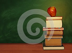 Back to school, pile of books and red apple with empty green school board background, education concept