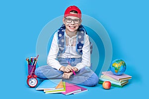 Back to school. Portrait of school girl in glasses sit floor on blue background.