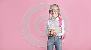 Back to school on September 1 concept. Smiling schoolgirl in glasses and backpack is holding books on pink background