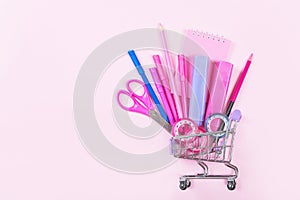 Back to school shopping concept. Colorful school supplies with shopping trolley on pink background.