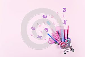 Back to school shopping concept. Colorful school supplies with shopping trolley on pink background.