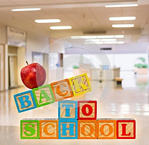 Back to School spelled out in wooden blocks with apple against corridor