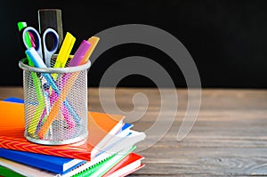 Back to school. Stack of books and school supplies on black board background. Education concept