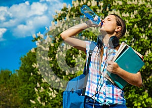 Back to school student teenager girl drinks water from a bottle and holding books and note books wearing backpack.