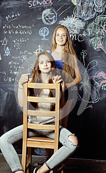 Back to school after summer vacations, two teen girls in classroom with blackboard painted together